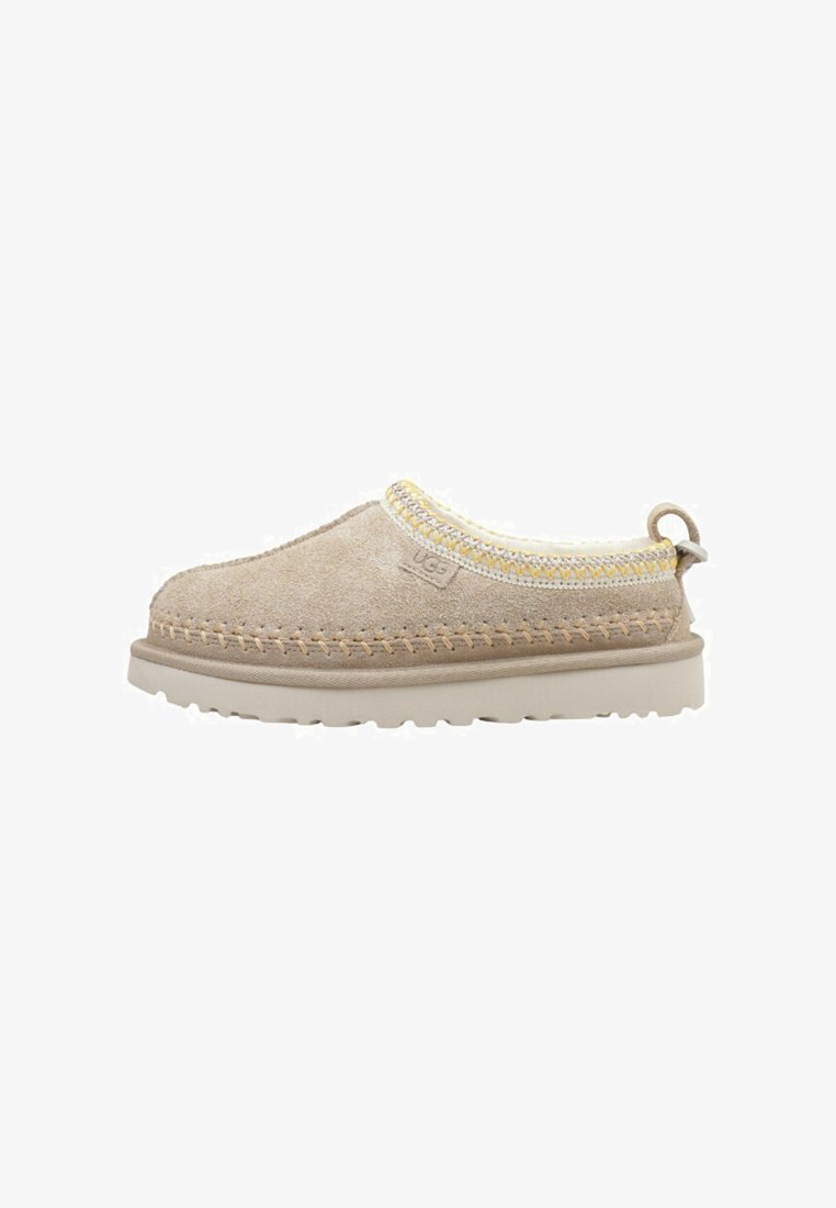 Chaussure en suède beige à enfiler avec une épaisse semelle beige, un bord cousu jaune et blanc, et une languette au talon.