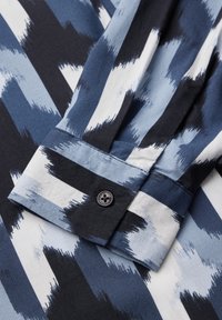 Maglietta con bottoni caratterizzata da un motivo astratto blu e bianco. Realizzata in tessuto leggero con un colletto distintivo e chiusura a un bottone sui polsini.