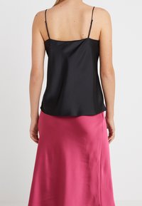 Svart satin camisole med tunna spännen, kombinerad med en rosa satin kjol, som har en slät yta och en lätt avslappnad passform.