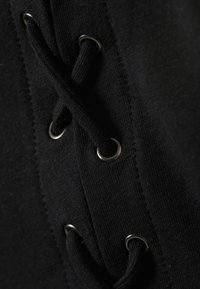 Nahaufnahme von schwarzem Stoff mit Metallösen, durch die eine schwarze Schnürsenkelschnur in einem Kreuzmuster gefädelt ist.