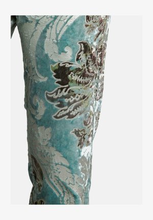 Türkisfarbener Samtstoff mit aufwendigen floralen Mustern in Silber und Braun. Die Textur ist weich und plüschig und zeigt detaillierte Stickereien.