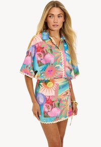 Ensemble de chemisier à manches courtes coloré et jupe assortie en bleu, comportant des motifs tropicaux, des flamants roses, des motifs de soleil et des bords festonnés.