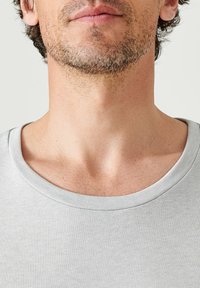 Maglietta in cotone grigio con un ampio scollo rotondo. La texture è liscia e aderente, con un sottile motivo a costine.