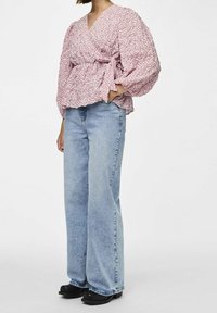 Blusa avvolgente rosa con motivo floreale e maniche a palloncino, abbinata a jeans a vita alta blu chiaro e a gamba larga, e scarpe nere.