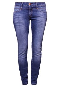 Vaqueros pitillo en denim azul oscuro con lavado desgastado. Cuenta con cinco bolsillos, cremallera y costuras en contraste de color naranja a lo largo de las costuras.