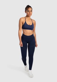 Reggiseno sportivo blu navy e leggings a vita alta realizzati in tessuto elastico. Presentano spalline sottili, un design aderente e un dettagli di branding discreto.