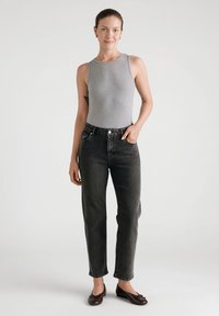 Szary bezrękawnik typu body, czarne jeansy z wysokim stanem i ciemnobrązowe baleriny, stojąca na neutralnym tle.