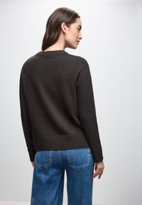 Dunkelgrauer Pullover mit rundem Ausschnitt, geripptem Saum und langen Ärmeln. Kombiniert mit blauen weitem Jeans. Einfacher, strukturierter Stoff.