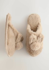Beige fluffy hjemmesko med en rund form, kaninører og pom-pom detaljer. Blød tekstur med slip-on design og flad sål.