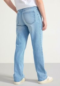 Lichtblauwe denim jeans met rechte pijpen, zichtbare achterzakken en een subtiele wassing, gecombineerd met witte sneakers.