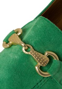 Groene suede instappers hebben een gouden kettingaccent met een getextureerd detail. De schoen heeft een gladde afwerking en een ronde vorm.