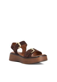 Brown suede sandals with two adjustable straps and gold buckles, featuring a chunky wooden platform and textured sole.
