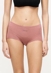 Γυναίκα που φοράει βαμβακερά μπόισορτ με υψηλή μέση σε μαβ απόχρωση, με την επιγραφή «Saturday» μπροστά και μαύρο κοντό τοπ σε λευκό φόντο.