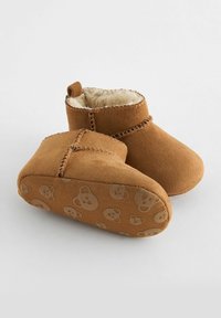 Bottines en suede marron avec une doublure intérieure douce, dotées d'une semelle texturée avec un motif répétitif de visage d'ours, d'une hauteur courte et d'accents cousus.