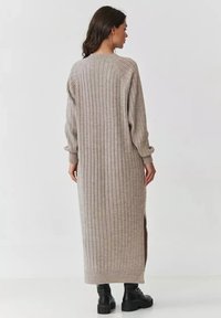 Długi, prążkowany kardigan w beżowym kolorze, z luźnym krojem, bocznymi rozcięciami i prążkowanymi mankietami, połączony z czarnymi botkami za kostkę.
