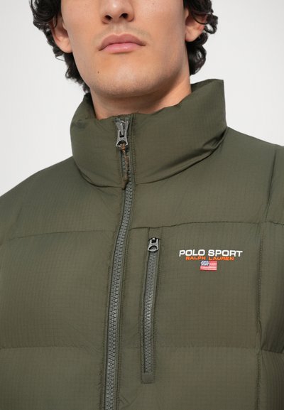Olivovo zelená nafukovacia bunda s vysokým golierom, predným zipsom a vreckom na hrudi. Obsahuje vyšívané logo "POLO SPORT" v bielej a oranžovej farbe.