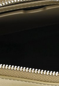 L'interno della borsa beige presenta una fodera liscia, una cerniera marrone chiaro a contrasto e dettagli di cucitura visibili su uno sfondo scuro.