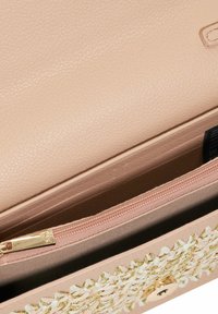 Lichtroze lederen tas met een gestructureerde afwerking, voorzien van een ritszak met gouden accenten en een bloemenborduurontwerp aan de voorkant.