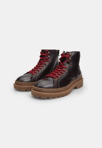 Stivaletti in pelle marrone con lacci rossi, punta tonda e suola gomma spessa. Presentano una zip sul lato e occhielli metallici.