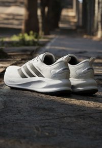Paire de baskets blanches et grises avec des semelles épaisses, placées sur une surface extérieure pavée sous une lumière naturelle douce.