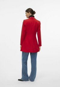 Czerwony blazer o dopasowanym kroju, z długimi rękawami i czarnym kołnierzem, w połączeniu z jasnoniebieskimi spodniami typu wide-leg i czarnymi butami.
