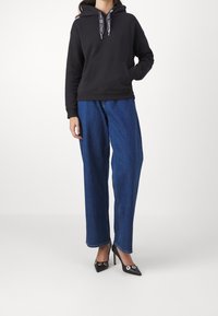 Black hooded sweatshirt with front pocket, paired with loose blue denim jeans and pointed black high heels featuring gold accents.