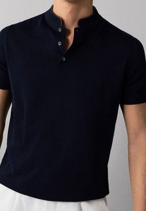 Mężczyzna ubrany w czarną koszulę henley z krótkim rękawem, stójką mandaryńską i trzema guzikami, w połączeniu z białymi spodniami.