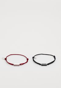 Deux bracelets en cordon ajustables, l'un rouge et l'autre noir, chacun avec une plaque rectangulaire en argent gravée "HUGO."