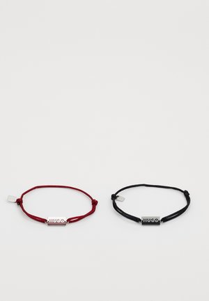 Due braccialetti in corda regolabile, uno rosso e uno nero, ciascuno con una placca rettangolare in argento incisa con la scritta "HUGO."
