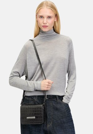 Sac en cuir noir à motif crocodile, porté en bandoulière, avec un accent en métal argenté. Le modèle porte un haut gris à manches longues avec un col montant et un jean sombre.