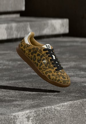 Leopardprintet sneaker med sorte snørebånd og brun sål, svævende over betontrapper i en udendørs omgivelser.