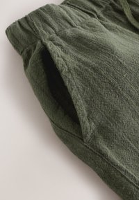 Close-up of a textured dark green fabric pants pocket with visible stitching and an elastic waistband.