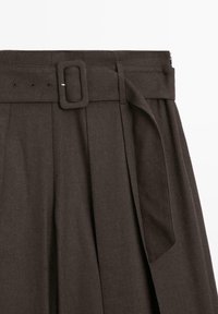 Donkerbruine geplooide broek met een brede tailleband en een rechthoekige gespsluiting. De stof heeft een gladde textuur, met lussen voor een riem en zijnaden aan de zijkant.