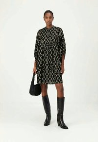 Rochie neagră cu un model geometric alb, croială lejeră, până la genunchi, cu talie strânsă. Asortată cu cizme negre înalte și o geantă texturată.