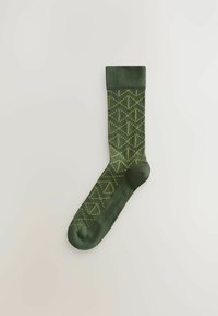 Chaussette verte avec un motif géométrique jaune, bord-côte, texture lisse et design de longueur cheville.
