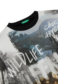 Bílá mikina s černým kulatým výstřihem, která má fotografický potisk přírody a text "WILDLIFE" a "VYBERTE SI DOBRODRUŽSTVÍ." Měkká textura.