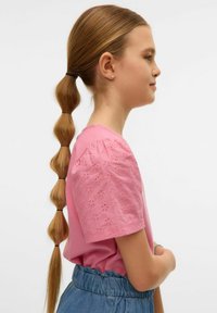 Różowa bawełniana koszulka z haftowanymi bufkami, połączona z jasnoniebieską spódnicą na elastycznej talii. Gładkie włosy stylizowane w długi warkocz.