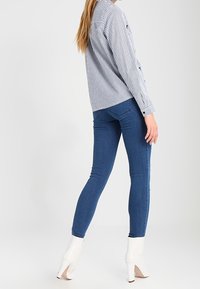 Chemise à rayures à boutons bleu clair et blanc, associée à un jean skinny bleu foncé et des bottines blanches à talons hauts.