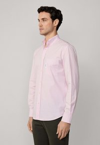 Camisa de manga larga a cuadros en color rosa claro con cuello abotonado, bolsillo en el pecho y botones amarillos. Textura de tela suave.