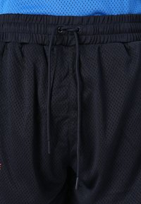 Svarte mesh idrettsshorts med elastisk midje og snøring. Har perforerte hull for pusteevne og en kontrast i stofftekstur.