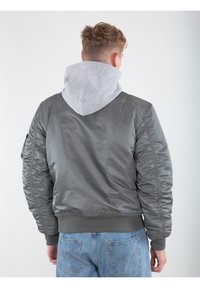 Giacca bomber grigia con fodera in felpa grigia, caratterizzata da polsini e orlo a costine e una texture del tessuto liscia e lucida.