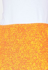 Falda a rayas en naranja y amarillo con una superficie texturizada, que cuenta con una cintura fruncida y una parte superior blanca lisa parcialmente visible arriba.