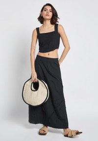 Črn top s kvadratnim izrezom, v kombinaciji z dolgo črno krilo z teksturiranim vzorcem. Bež krožna tkanina torba in svetlo rjave sandale.