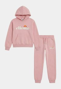 Sweat à capuche rose de la marque ellesse avec une poche kangourou à l'avant et pantalon de jogging assorti doté d'une taille à cordon de serrage et du logo sur la cuisse gauche.