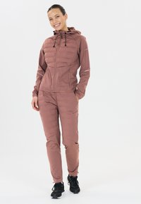 Gevoerde roze buitenjas met capuchon en trekkoorden, gecombineerd met bijpassende broek. Beide hebben een gladde, waterafstotende textuur.
