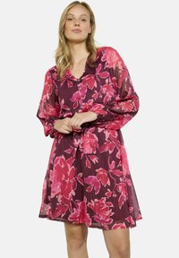 Vestido floral con una base burdeos profunda y patrones florales vibrantes en rosa. Presenta mangas largas, un escote en V y un lazo en la cintura.