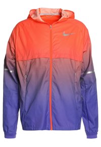 Chaqueta cortavientos Nike en colores degradados, que pasan de coral brillante a púrpura. Cuenta con cremallera frontal, capucha y detalles reflectantes.