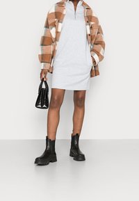 Brun och vit rutigt flanelljacka över en grå zip-up klänning, matchad med svarta kraftiga klackstövlar och en liten svart handväska.