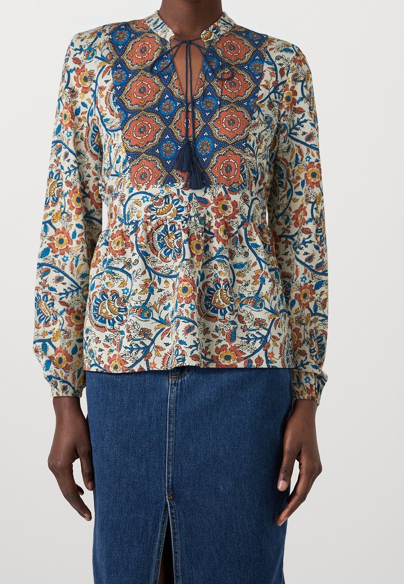 Blusa a fantasia floreale multicolore con scollatura a chiave, dettagli blu e frange. Maniche lunghe e vestibilità comoda.