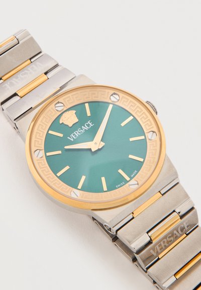 Ρολόι χειρός Versace με μπάντα από χρυσό και ασημί μέταλλο, πράσινο καντράν, χρυσούς δείκτες ωρών και το λογότυπο της Μέδουσας στη θέση 12.